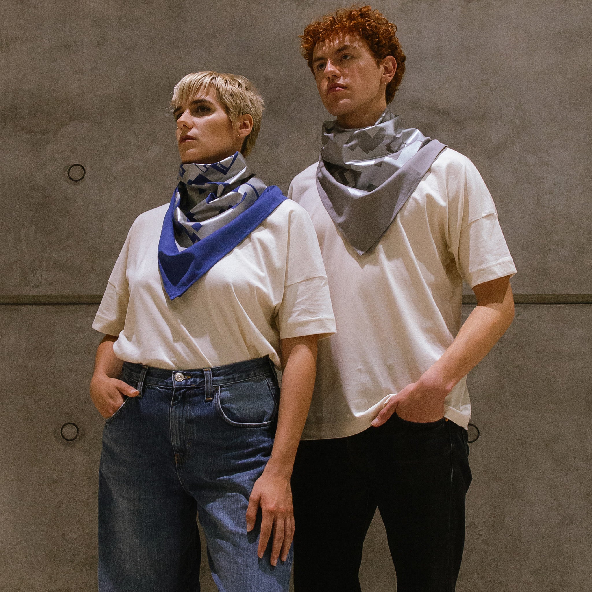 Eine Frau und ein Mann, tragen beide ein großes Bandana in blau und grau um den Hals. Auf dem Bandana ist ein großflächiger Foliendruck in grau zu sehen.