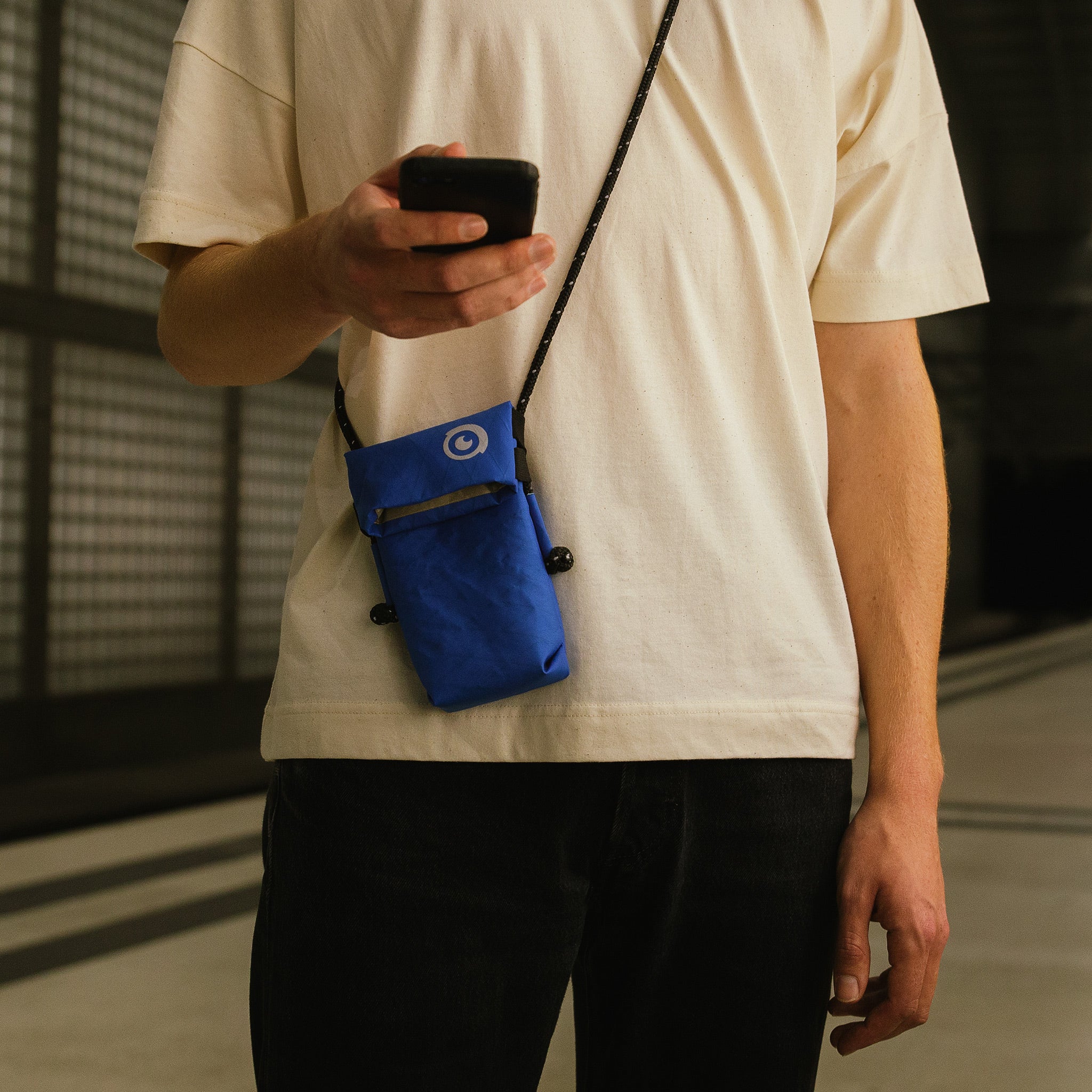 Ein Mann hält sein Handy in der Hand und trägt eine blaue abschirmende Umhängetasche von Urbanprivacy