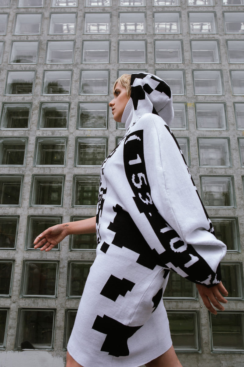 Frau mit schwarz weiß gemusterten Strickkleid, in Pixeloptik, trägt eine Kapuze und läuft