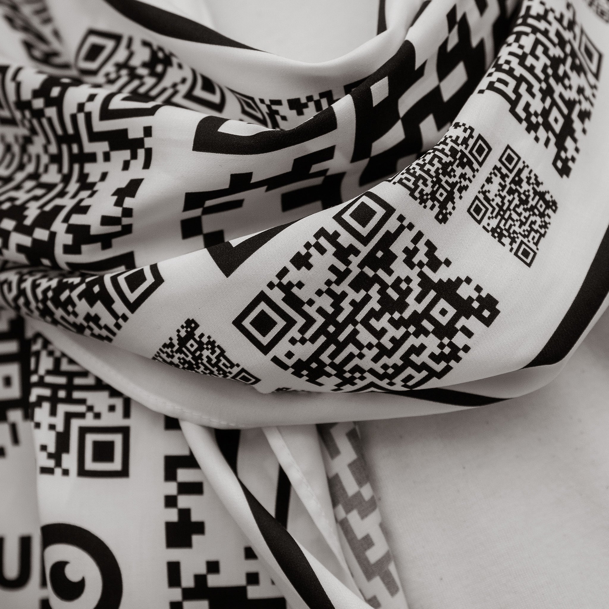 Detailaufnahme eines Schals. Auf dem Schal sind viele schwarz weiße QR-Codes in unterschiedlichen Größen zu sehen.