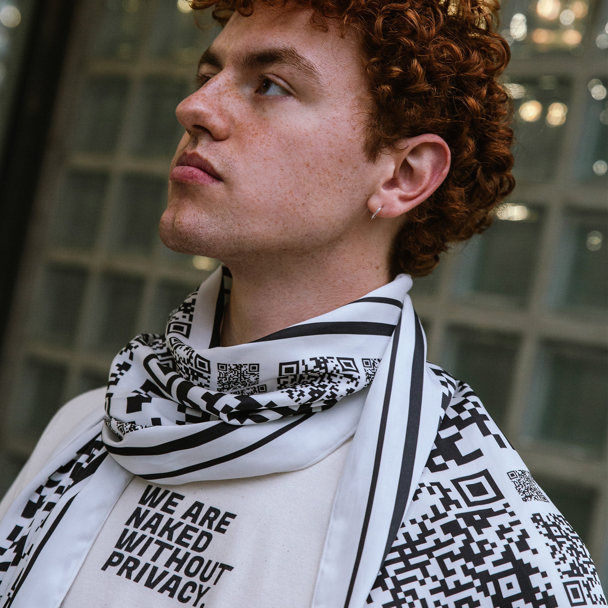 Mann mit einem Schal aus Tencel. Auf dem Schal sind viele schwarz weiße QR-Codes in unterschiedlichen Größen zu sehen.