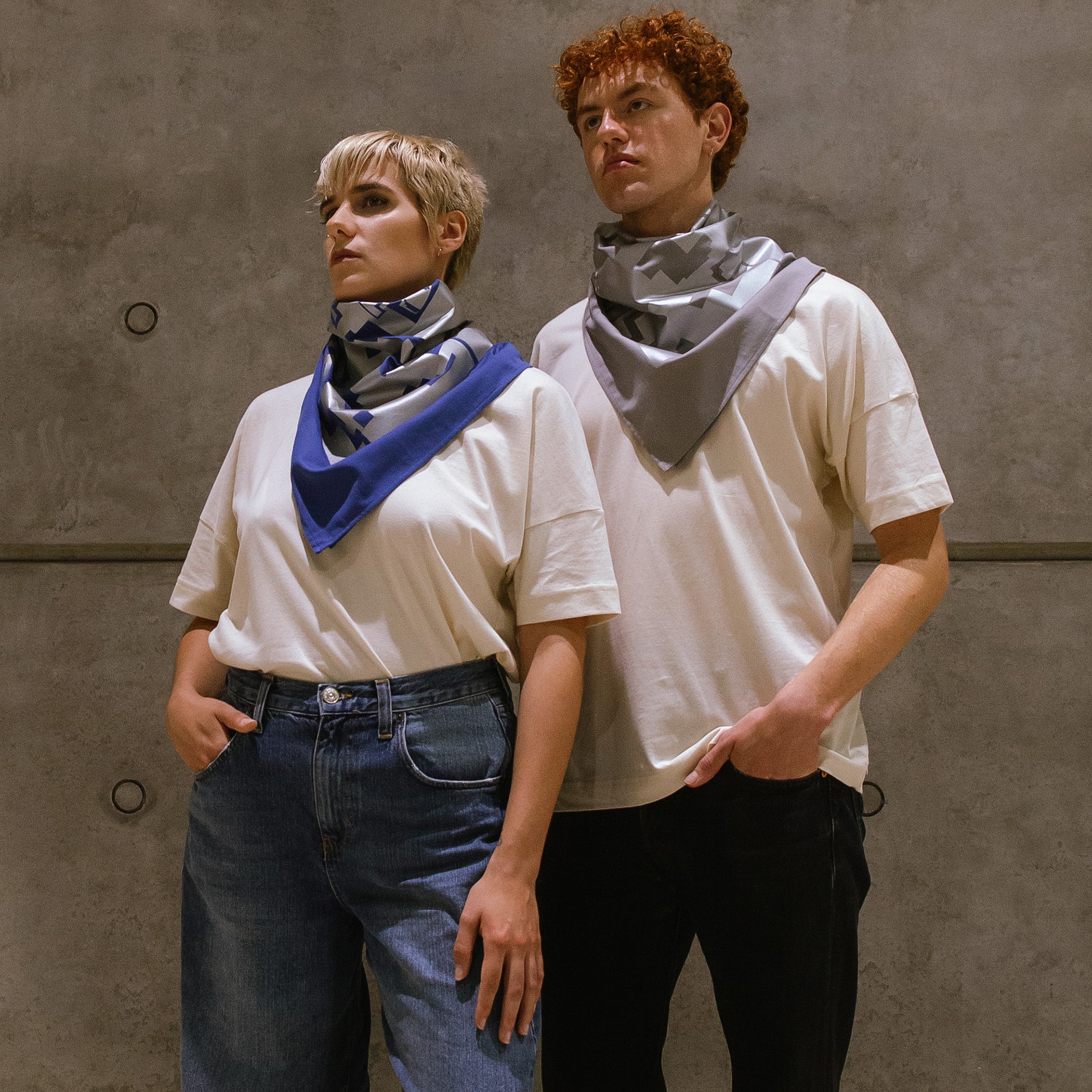 Eine Frau und ein Mann, tragen beide ein großes Bandana in blau und grau um den Hals. Auf dem Bandana ist ein großflächiger Foliendruck in grau zu sehen. 